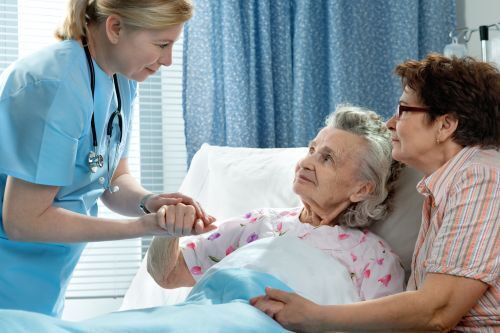a old woman in a hospital bed holding hand with a nurse.