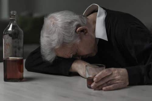 elderly man with his head down on the table with a glass of alcohol.