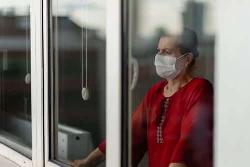 A woman with a mask looking through a window at a nursing home.