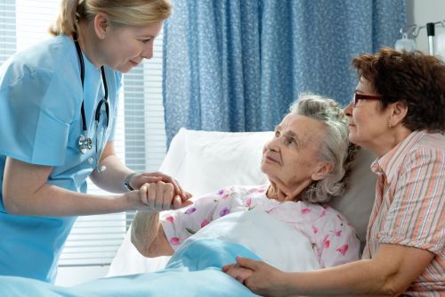 a nurse holding a patients hand in a hospital bed.